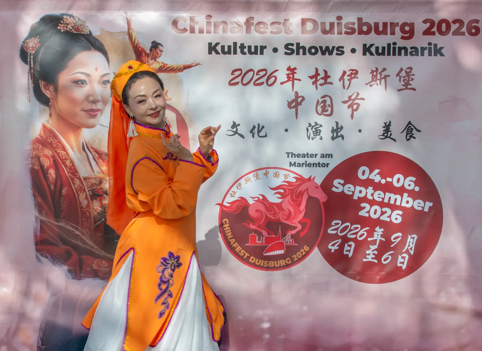 Tänzerin in orange-weißem Gewand posiert vor dem Festbanner am Düsseldorfer Burgplatz
