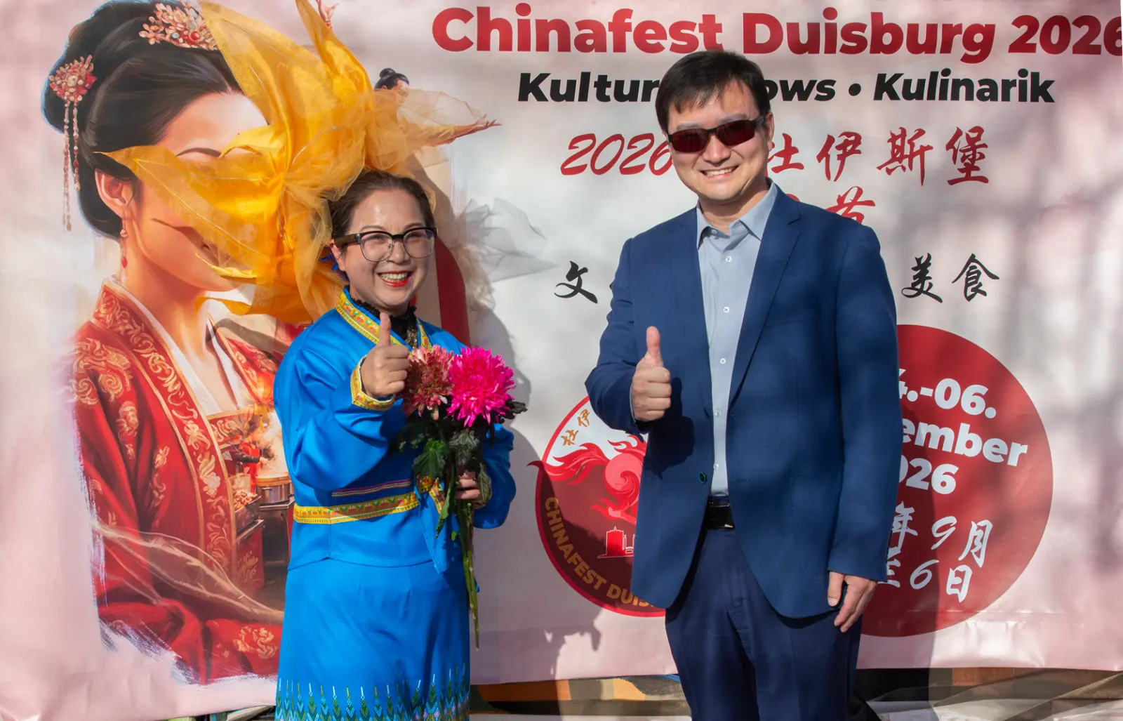 Huiying Tang in blauer Tracht und Generalkonsul Yu Yong vor dem Banner des Chinafests Duisburg 2026